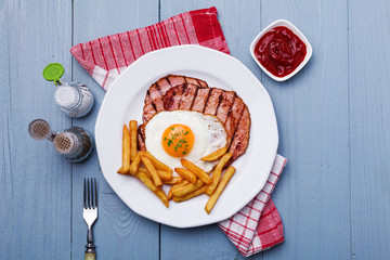 English breakfast with grilled ham, fried egg and french fries.