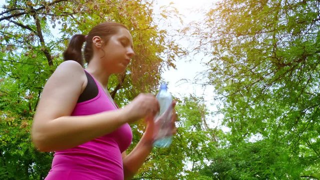 A young woman runs and drinks water in a beautiful green park in slow motion, 4 K Video Clip