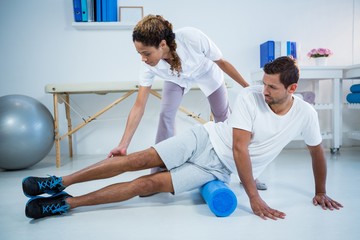 Physiotherapist doing leg therapy to a man using foam roll