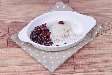 Black bean and sticky rice in sweet coconut cream topped coconut milk on gray and wood. Side view
