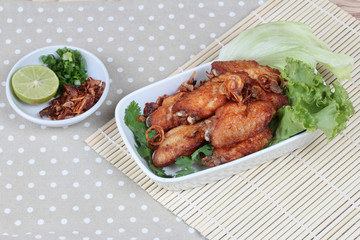 Deep fried chicken topped fried sliced red onion served with side dish as halve green lemon ,minced shallots and filled fried red onion on bamboo and gray. Side view.