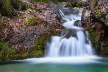 Fototapeta na wymiar Cascata nella roccia con acque bianche effetto seta che finiscono in un lago verde smeraldo