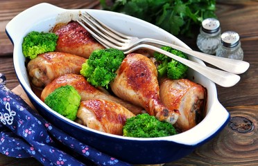 Baked chicken drumstick with organic broccoli on a wooden background.
