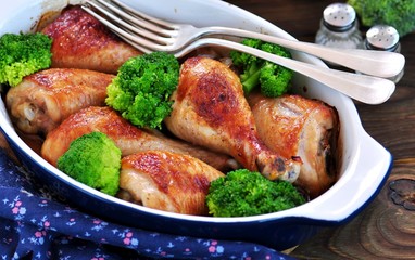 Baked chicken drumstick with organic broccoli on a wooden background.