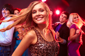 A young blond dancing, looking at camera and smiling against her four friends