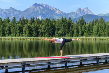Frau macht Balance- und Kräftigungsübung auf einem Steg am See