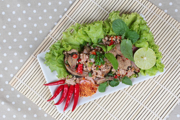 Spicy and sour mixed herb salad with pork and chicken on bamboo and gray. Top view.