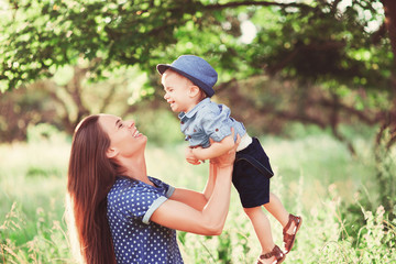 Fototapeta premium Loving mother holding son in her arms, plays with him and hugs him. Family rest on the nature. soft focus