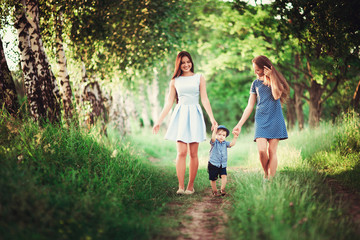 Fototapeta premium Beautiful happy family resting in nature. Two women - mother and aunt are the boy's hand along the trail in the woods. soft focus