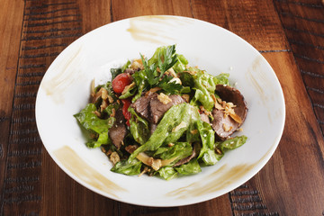 Salad with roast beef in a white plate. Brown wooden background