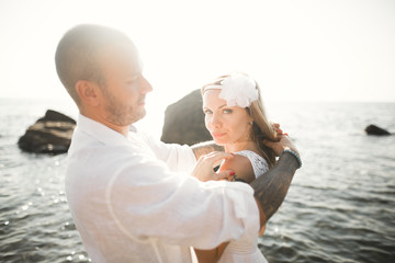 Romantic loving couple posing on stones near sea, blue sky