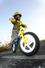 Obraz premium Baby boy riding on his first bike. Bike without pedals. Child learning to ride and balance on his two wheeler bike with no pedals.