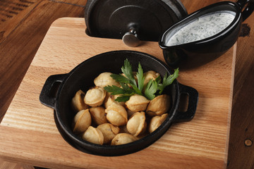 Fried meat dumplings (pelmeni, chuchpara) in a black pan. wooden background.