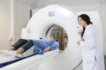 Patient Lying On MRI Machine While Female Doctor Operating It