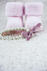 Fototapeta na wymiar Two pink booties for babies with several bracelets on the white fur