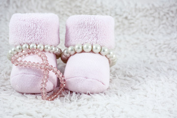 Pink booties for babies with several pink bracelets on the white fur
