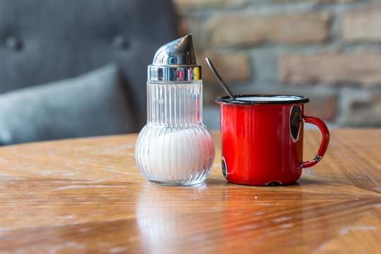 Old Red Enamel Cup And Modern Sugar Shaker On A Table