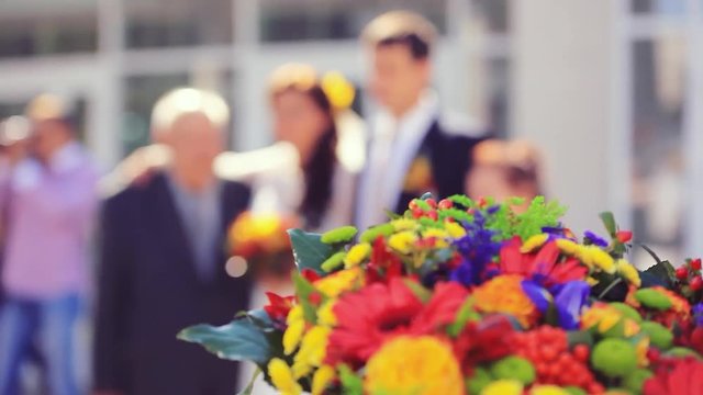Wedding focused bouquet in the foreground and blurred of newlywed couple having fun in green sunny park. 1920x1080