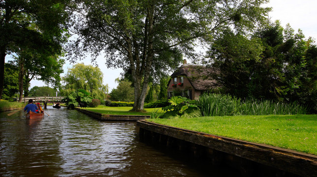Giethoorn, The Netherlands - July 10, 2016: Unknown visitors in the sightseeing boating trip in a canal in Giethoorn. The beautiful houses and gardening city is know as "Venice of the North".