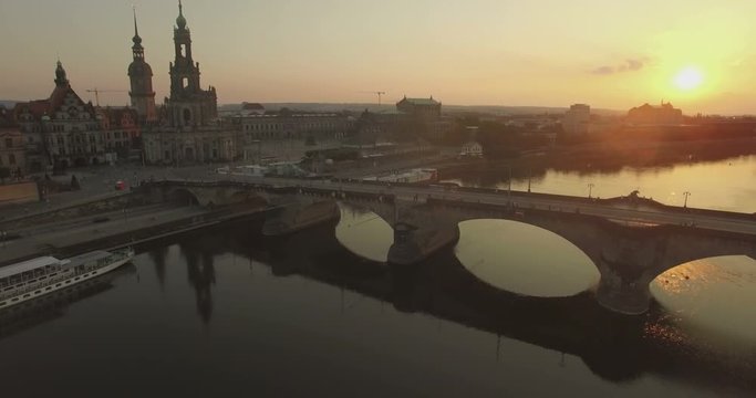 Aerial camera descends over the Elbe River with Katholische Hofkirche and the Augustusbruke in shot.The sun is setting in the background