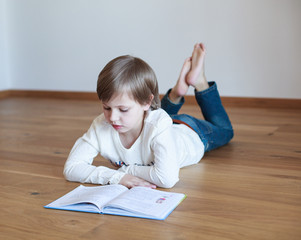 Naklejka premium Cute boy doing homework, he is lying on the floor and reading book 