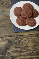 A plate of chocolate chip biscuits on a rustic wooden background forming a page border