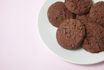 A plate of freshly baked chocolate chip cookies on a pastel pink background