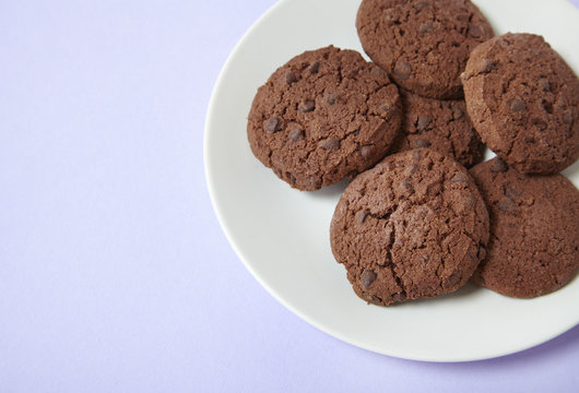 A plate of freshly baked chocolate chip biscuits on a pastel purple background forming a page border