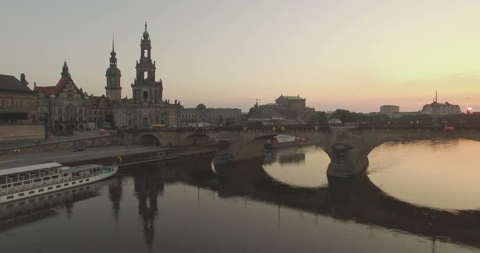 Aerial camera rises over the Elbe River with Katholische Hofkirche and the Augustusbruke in shot.The sun is setting in the background