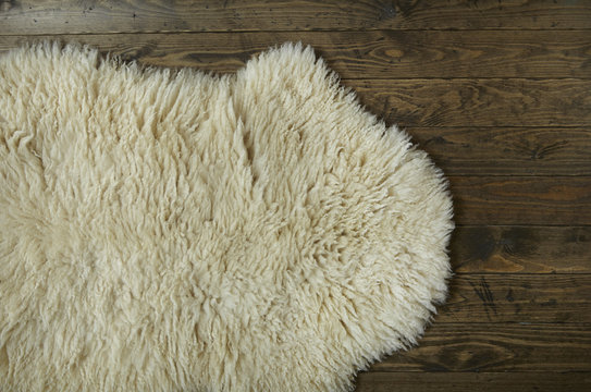 An aerial view of a cosy white sheepskin rug on a distressed wooden floor background