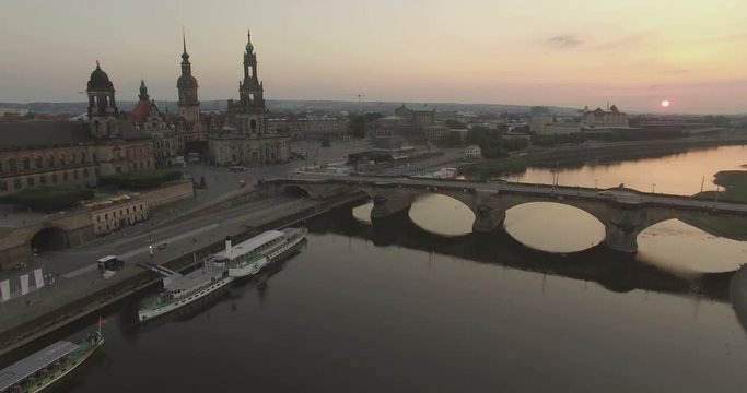 Aerial camera descends over the Elbe River with Katholische Hofkirche and the Augustusbruke in shot.The sun is setting in the background