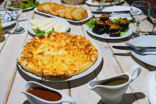  Table with traditional georgian food: hachapuri, tkemali souce, eggplant, salad, cheese, chadi. Selective focus