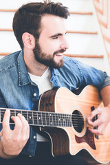 Handsome young man wearing a jeans shirt playing guitar. Music, instrument education, entertainment, pop rock star, music concert and learning concept