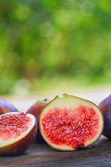 Fresh ripe black figs on rustic grey wooden table with green blurry background. Copy space