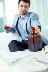 Depressed businessman reaching for bottle of cognac on his work desk
