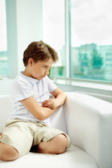 Obraz na płótnie Canvas Little sulky boy sitting on sofa