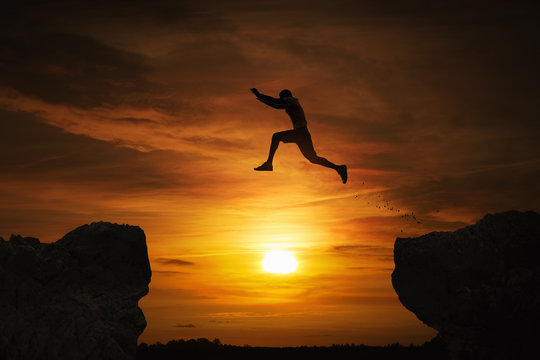 Silhouette of a man jumping over abyss at sunset with copy space