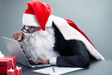 Santa Claus sitting at the table and pointing at laptop