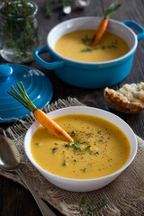 Carrot soup, served with roasted carrots, cream and fresh thyme on rustic background