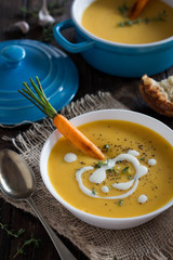 Carrot soup with roasted carrots, cream and fresh thyme on rustic background