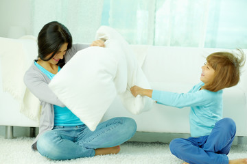Obraz premium Mother and her little daughter fighting with pillows at home
