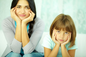 Portrait of mother and daughter looking at camera with hands on cheeks