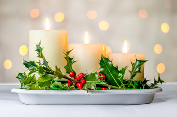 Christmas candles and holly berries with bokeh background.
