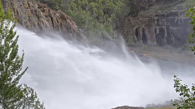 Wild and exciting scene. Water falling, strongly, by spillway of a dam, over the river. While a group of people is ready to do rafting. Cloudy day.