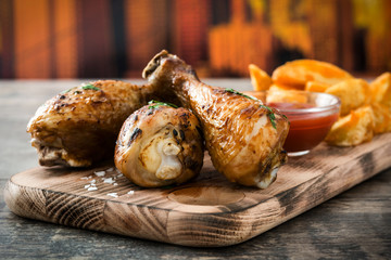Roast chicken drumsticks and chips on wooden background

