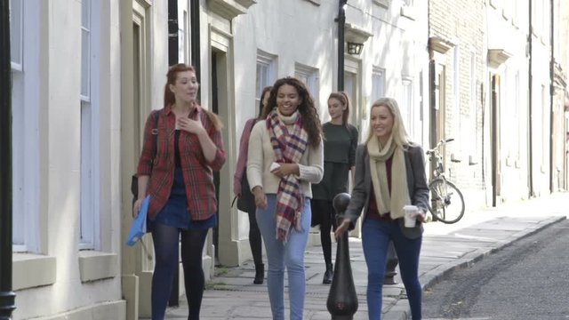 Group of girl students walking through the city. They are wearing casual clothing, smiling and holding educational materials.