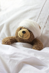 Teddy bear in bed with bandage on head