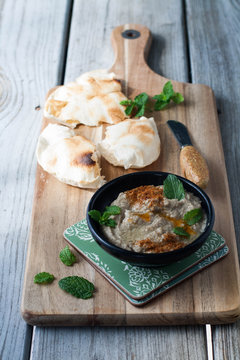 Baba ganoush with mint and pita bread on a wooden board. 