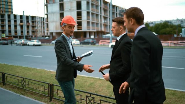 4k. Ultra HD. Two customers discontent architect work. Text pad. calculations. worker with helmet in suit and outdoors on new house building blueprints with crane and beams at bg housing industry