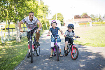 Naklejka premium Dad With Daughter Son Riding Bikes In Park